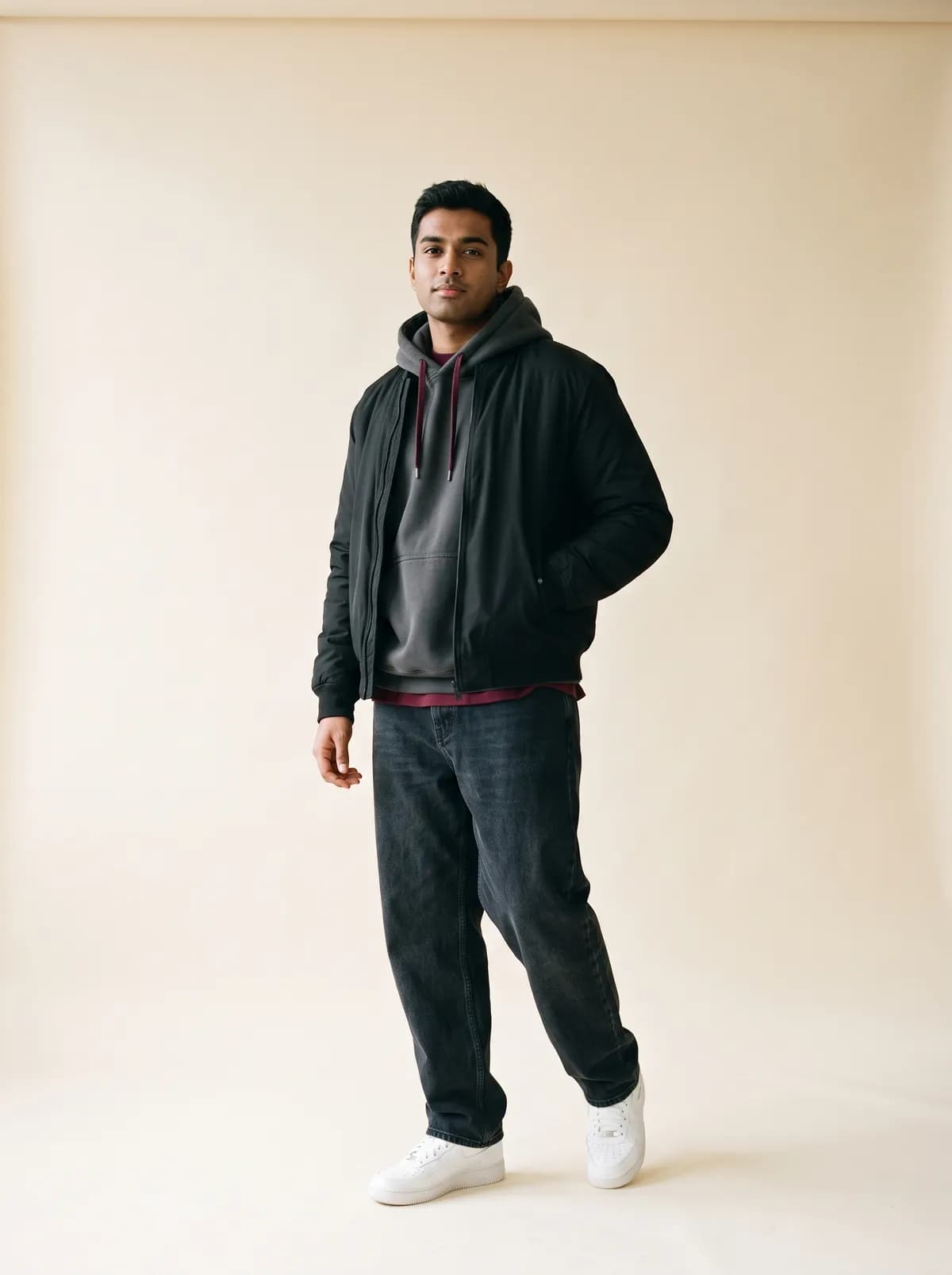 Hombre con bomber negra, sudadera gris y vaqueros anchos